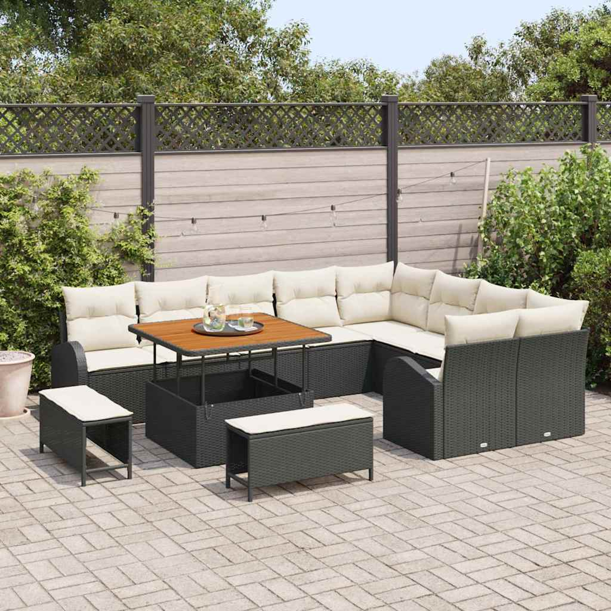 Outdoor-Ecksofa mit beigefarbenen Kissen, Holztisch und zwei Ottomanen auf einer Ziegelterrasse, vor einem Holzzaun und Grün.