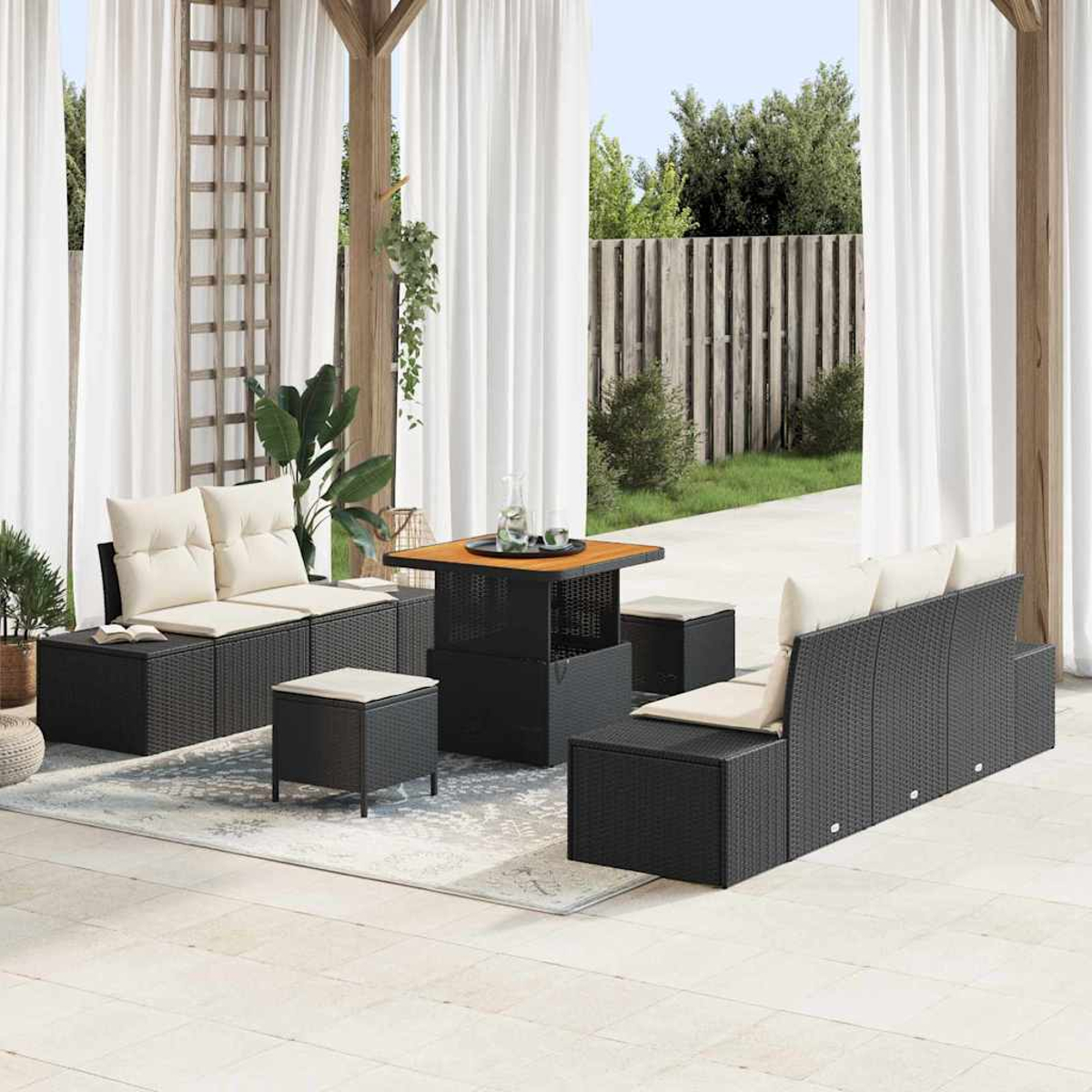 Outdoor-Sitzbereich mit schwarzem Korbmöbel, beigen Kissen, einem Tisch und weißen Vorhängen im Hintergrund.