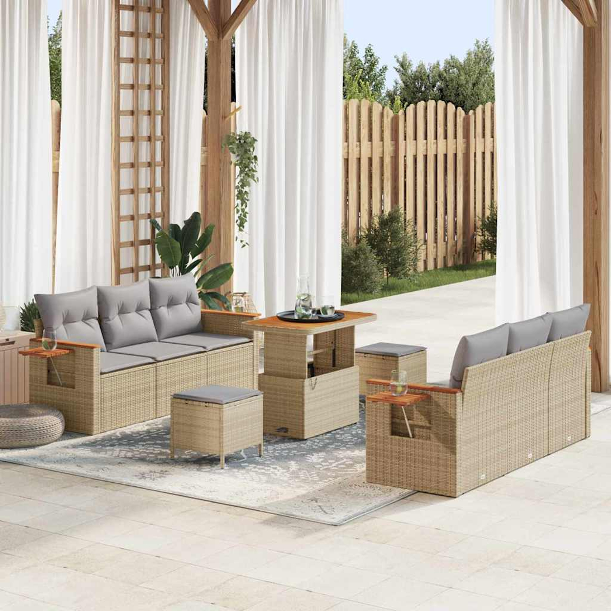 Terrassengarnitur mit beigefarbenen Korbs Sofas, grauen Kissen, einem Hubtisch und Ottomanen. Der Hintergrund zeigt Vorhänge und einen Holzzaun.