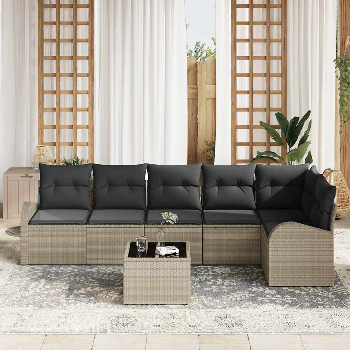 Ein Sitzbereich im Freien mit einem grauen Ecksofa, einem kleinen Tisch und einem gemusterten Teppich. Der Hintergrund zeigt weiße Vorhänge.