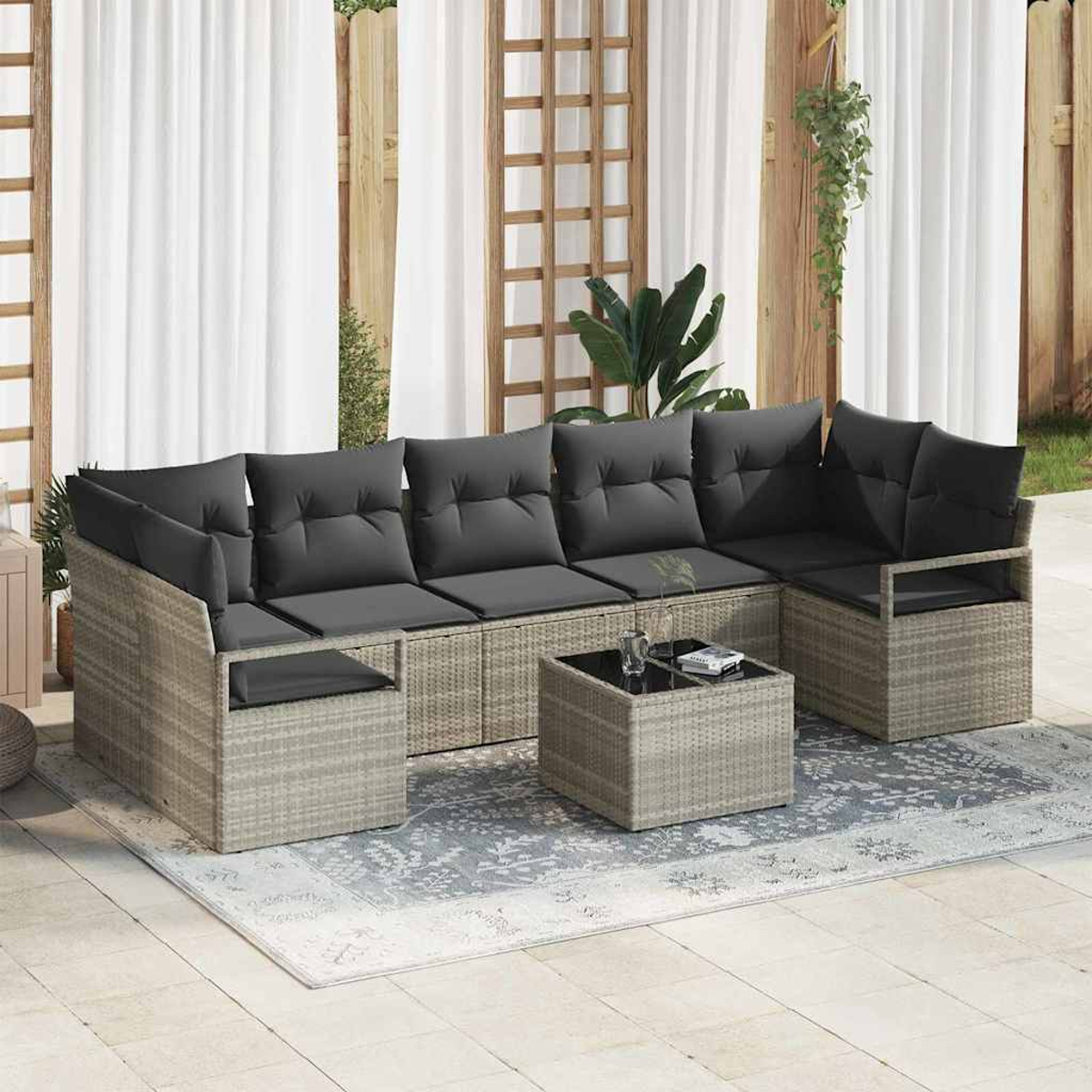 Outdoor-Ecksofa mit grauen Kissen und einem quadratischen Couchtisch, auf einem gemusterten Teppich, mit Vorhängen und Holzzaun im Hintergrund.