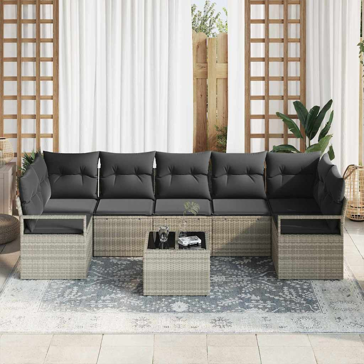 Outdoor-Ecksofa mit grauen Kissen, einem kleinen Tisch und einem Teppich. Im Hintergrund weiße Vorhänge und Holzgitter.