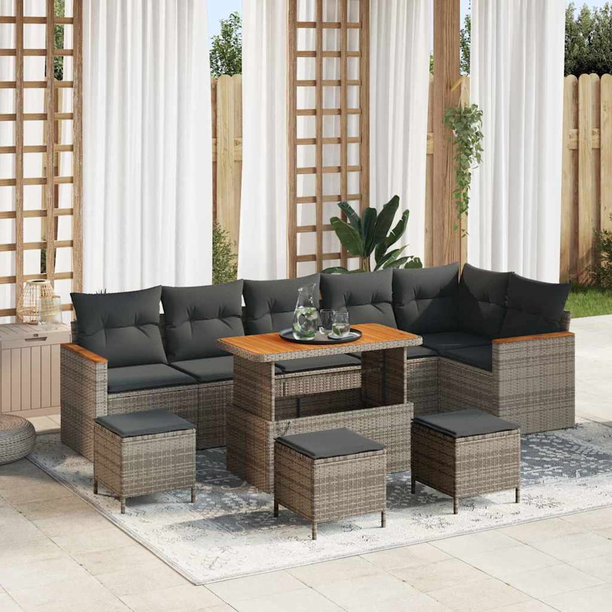 Gartenmöbel-Set mit grauen Kissen, Holztisch und passenden Hockern. Weiße Vorhänge und ein Holzzaun im Hintergrund.