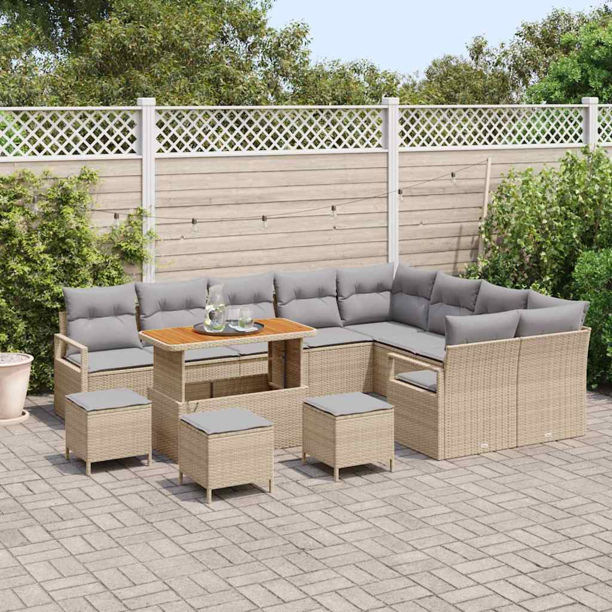 Gartenmöbel-Set aus Korbgeflecht mit grauen Kissen auf einer Terrasse. Enthält einen Tisch, ein Ecksofa und Hocker vor einem Zaun.