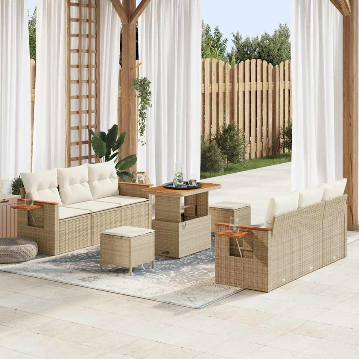 Juego de patio al aire libre con sofás beige, una mesa y otomanas. Cortinas blancas enmarcan la escena. Una valla de madera y vegetación al fondo.