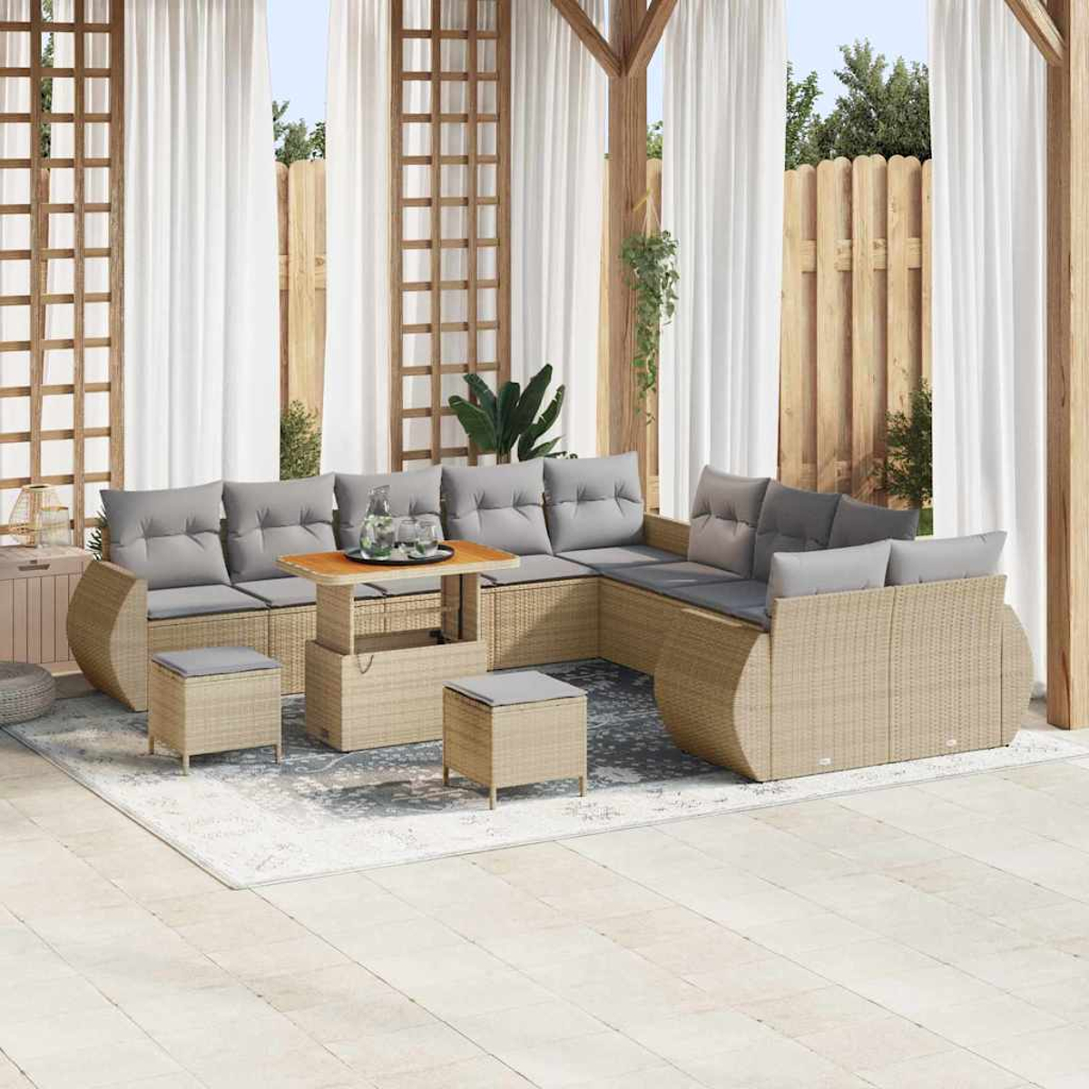 Zona de estar al aire libre con un sofá seccional de mimbre beige, cojines grises y una mesa de madera. Cortinas y valla al fondo.