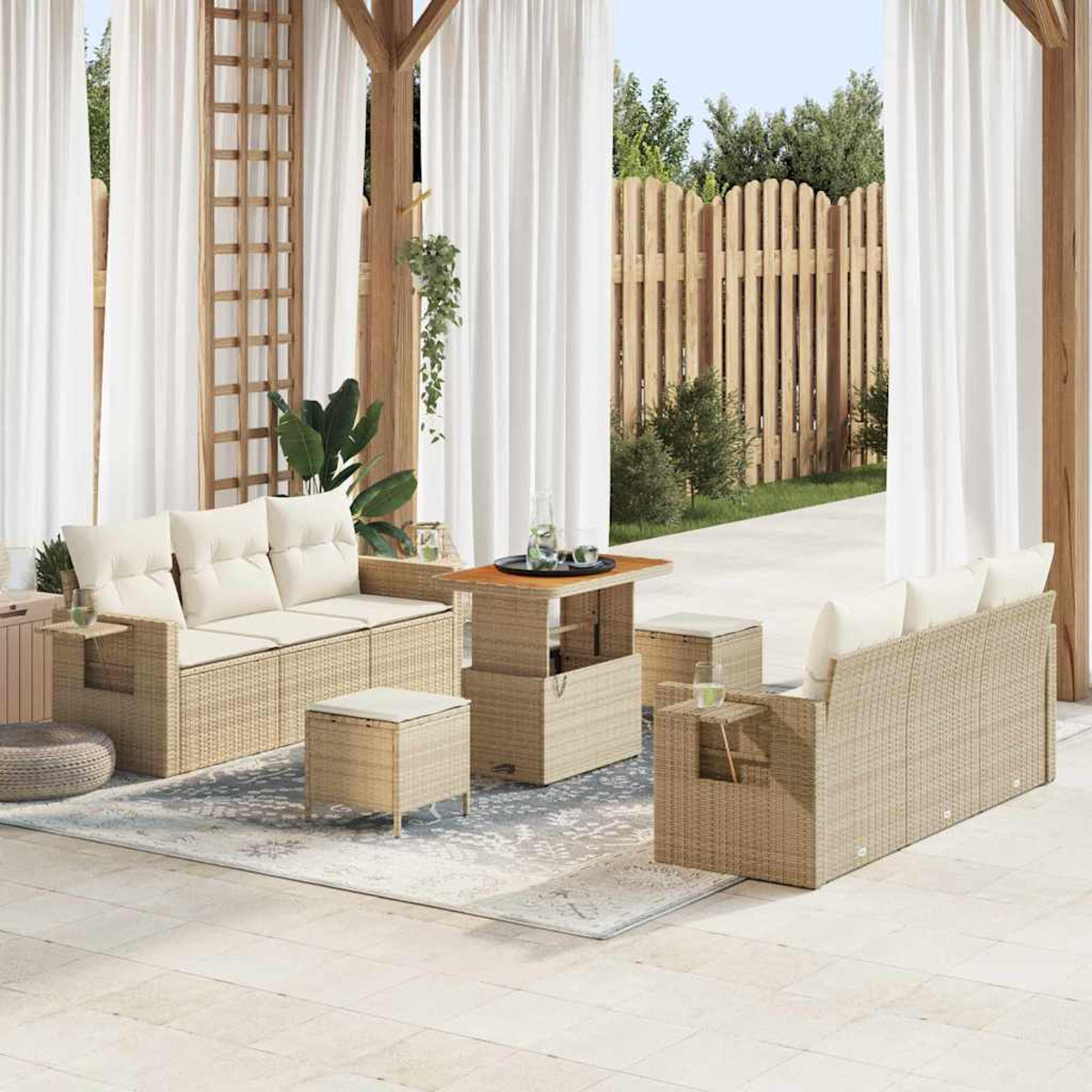 Terrassenset mit beigen Rattansofas, Couchtisch und Ottomanen. Weiße Vorhänge, Holzzaun und Pflanzen im Hintergrund.