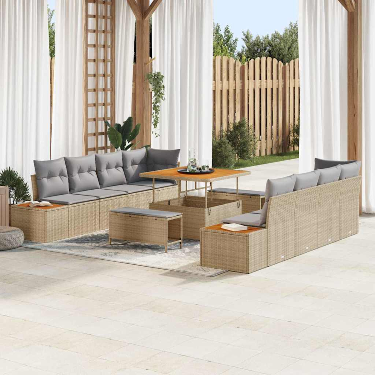 Terrassen-Set mit Korbs Sofas, grauen Kissen, Holztisch und weißen Vorhängen. Im Hintergrund ein Holzzaun.