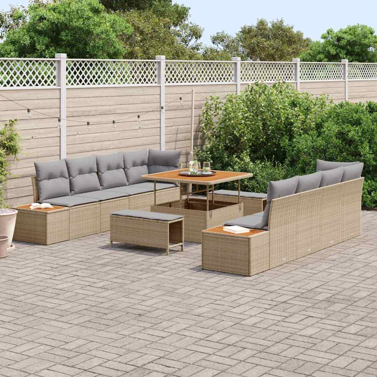 Outdoor-Sitzgruppe auf einer Terrasse. Enthält Sofas, Tisch und Bänke. Beige Korbmöbel mit grauen Kissen. Grüne Büsche und weißer Zaun.