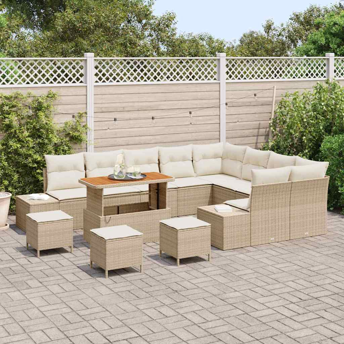 Terrassenmöbel-Set im Freien mit beigen Kissen, einem Holztisch und mehreren Ottomanen. Vor einem weißen Zaun und Grün.