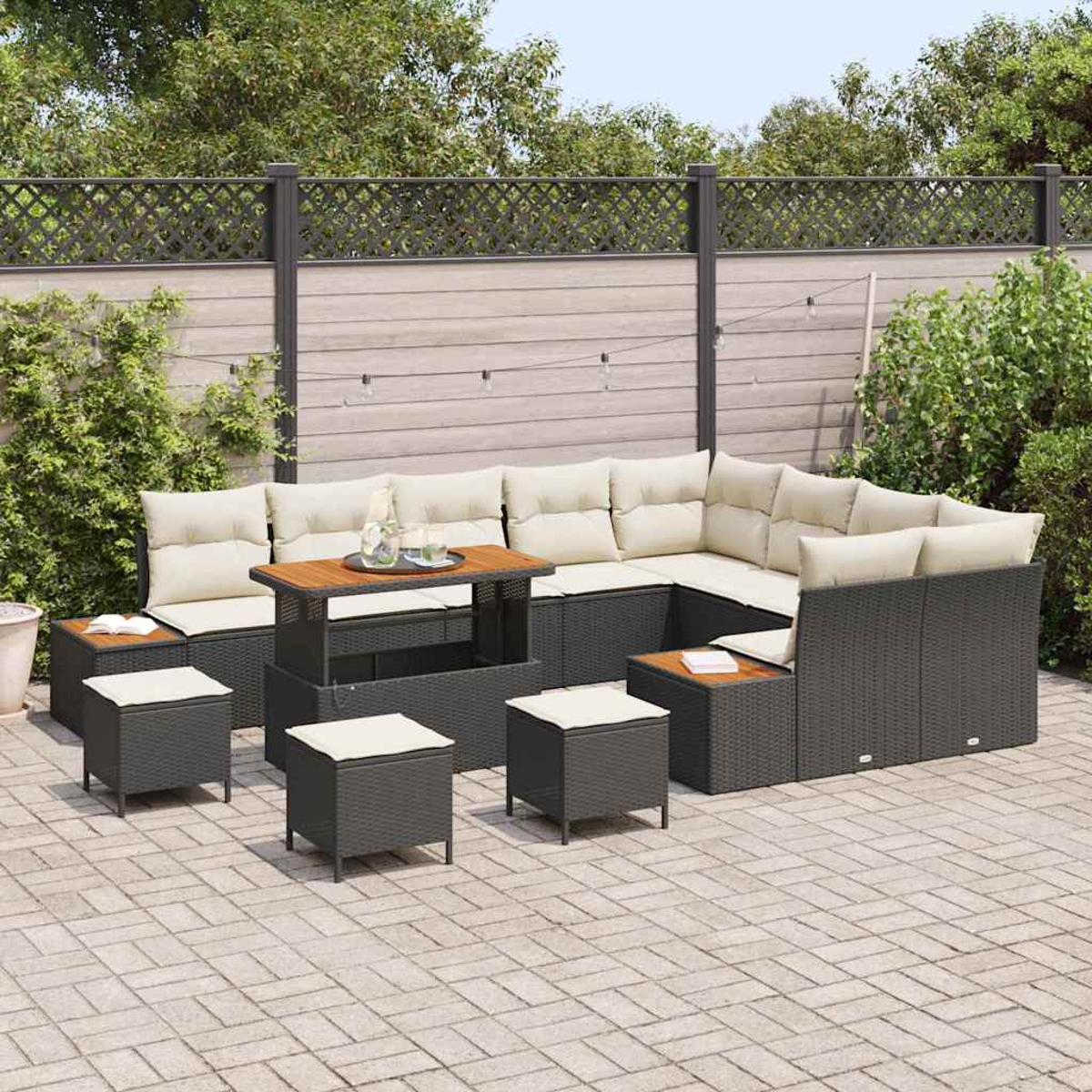 Juego de muebles de patio. Sofá seccional de mimbre gris oscuro con cojines beige, taburetes pequeños y mesa de madera en patio pavimentado.