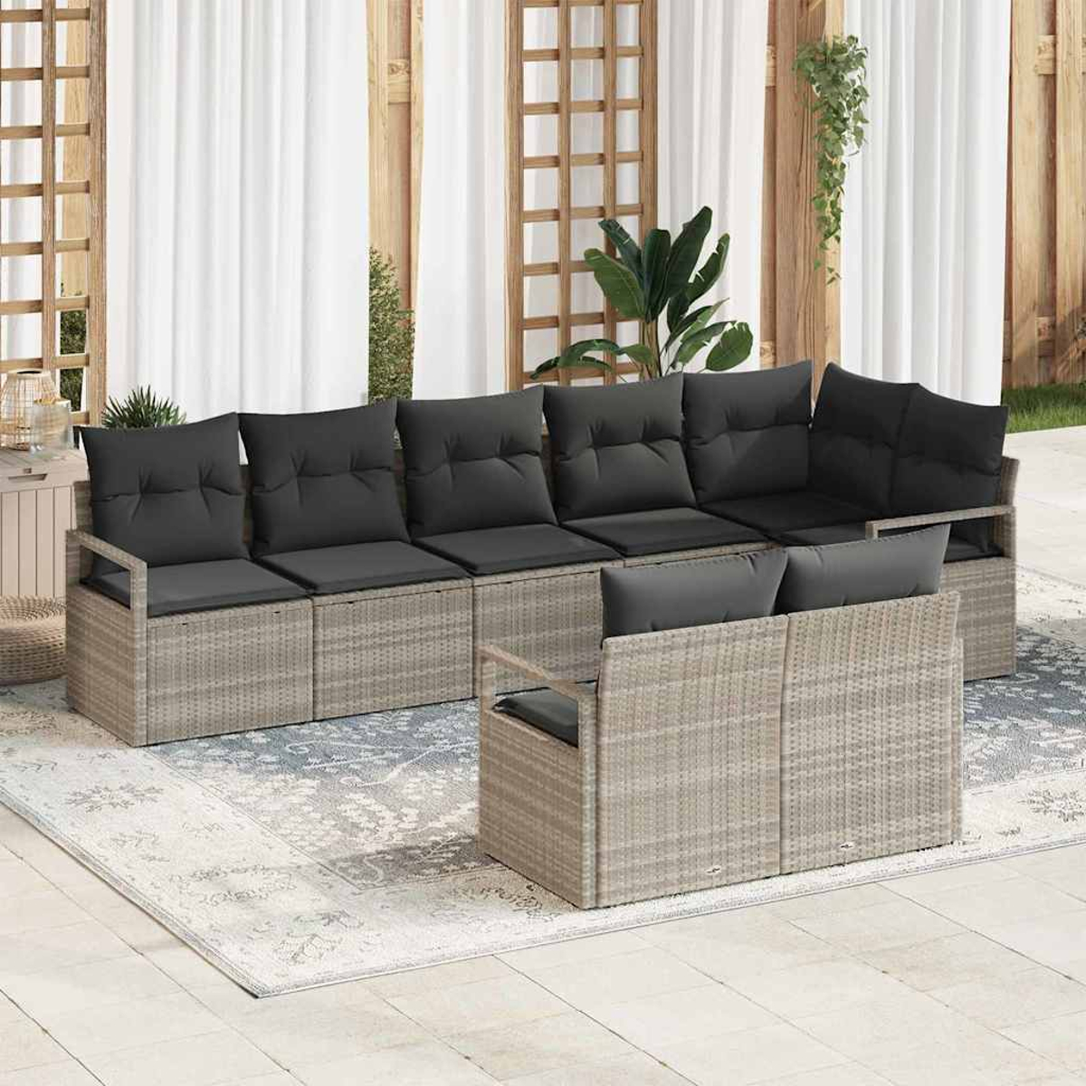 Geflochtenes Outdoor-Sofa mit schwarzen Kissen auf einem Teppich. Hintergrund: Vorhänge, Holzpaneele und Pflanzen, für eine Terrasse.