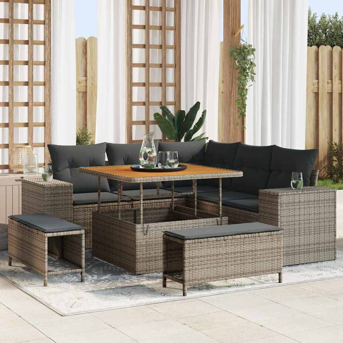 Garten-Terrassenset mit grauen Kissen, Holztisch, Korbmöbeln und weißen Vorhängen. Eine Kanne und Gläser stehen auf dem Tisch.