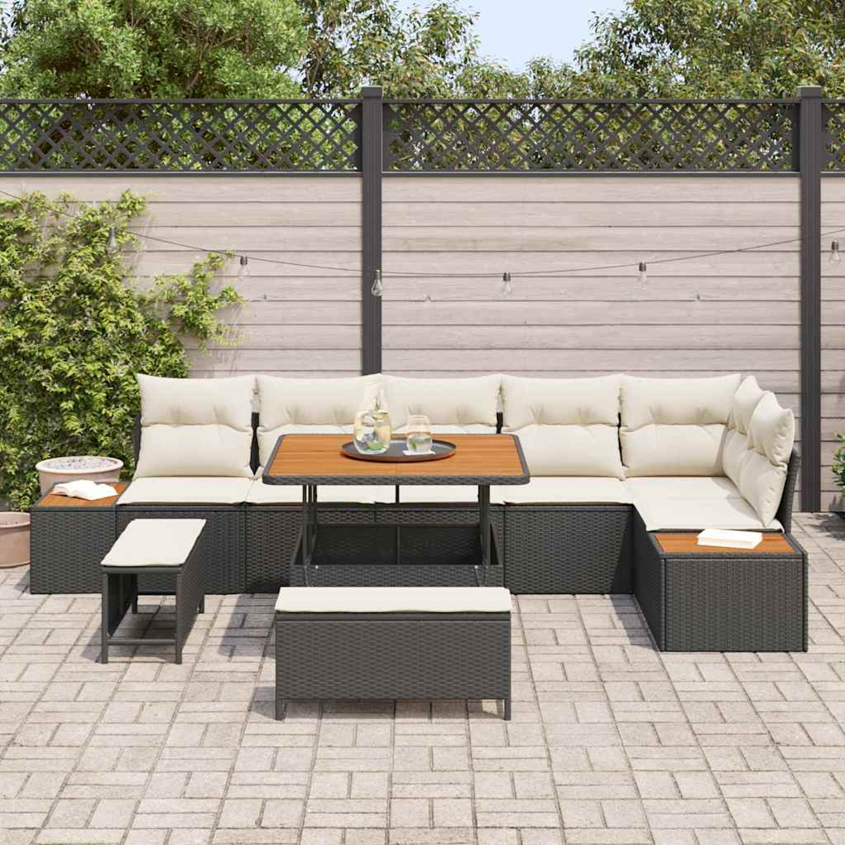 Gartenmöbel-Set: dunkles Korbmöbel-Sofa mit cremefarbenen Kissen, Holztisch und Bank. Umgeben von einem Zaun.