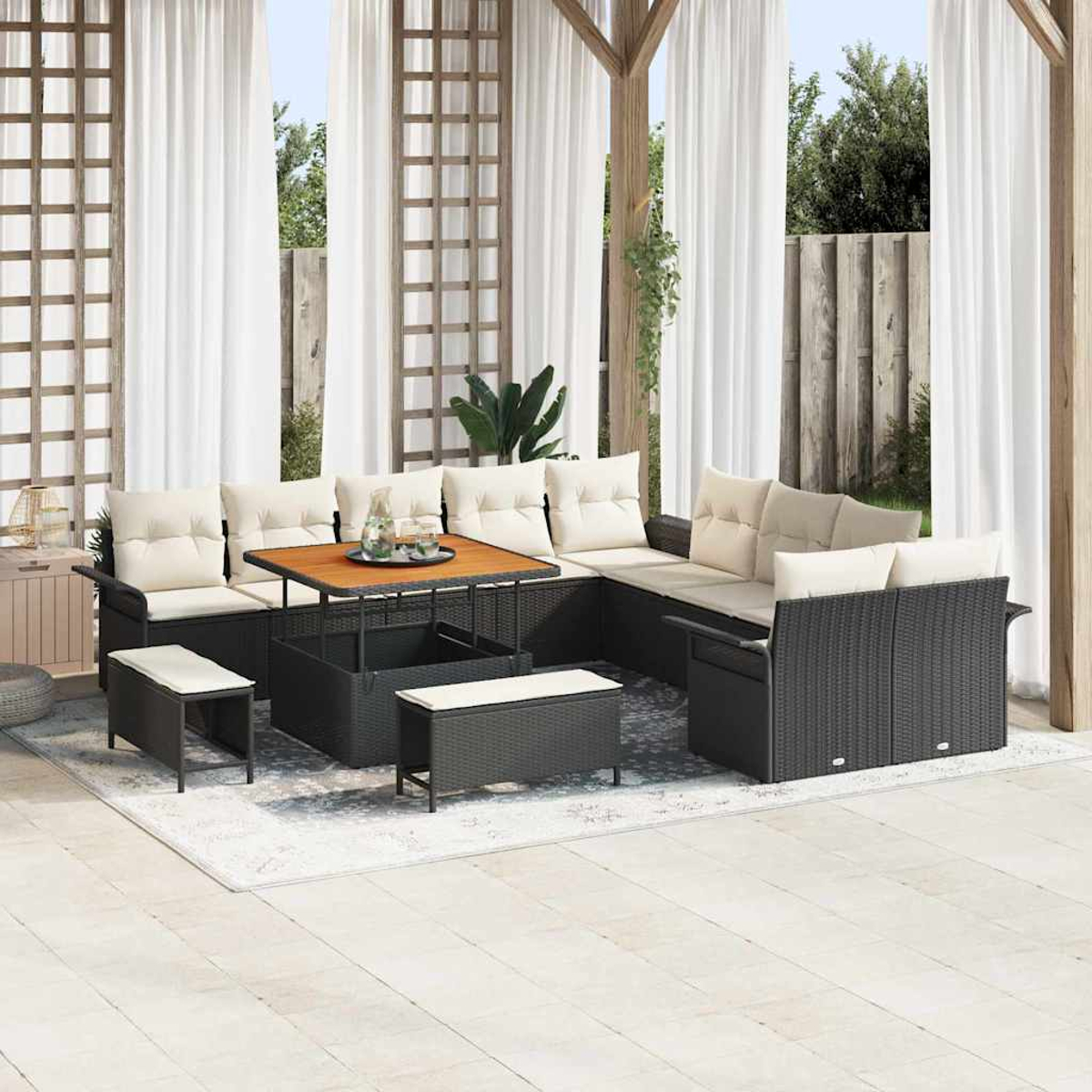 Garten-Sofa-Set mit schwarzem Korbmöbeln, beigen Kissen und einem Holztisch. Weiße Vorhänge und Grün im Hintergrund.
