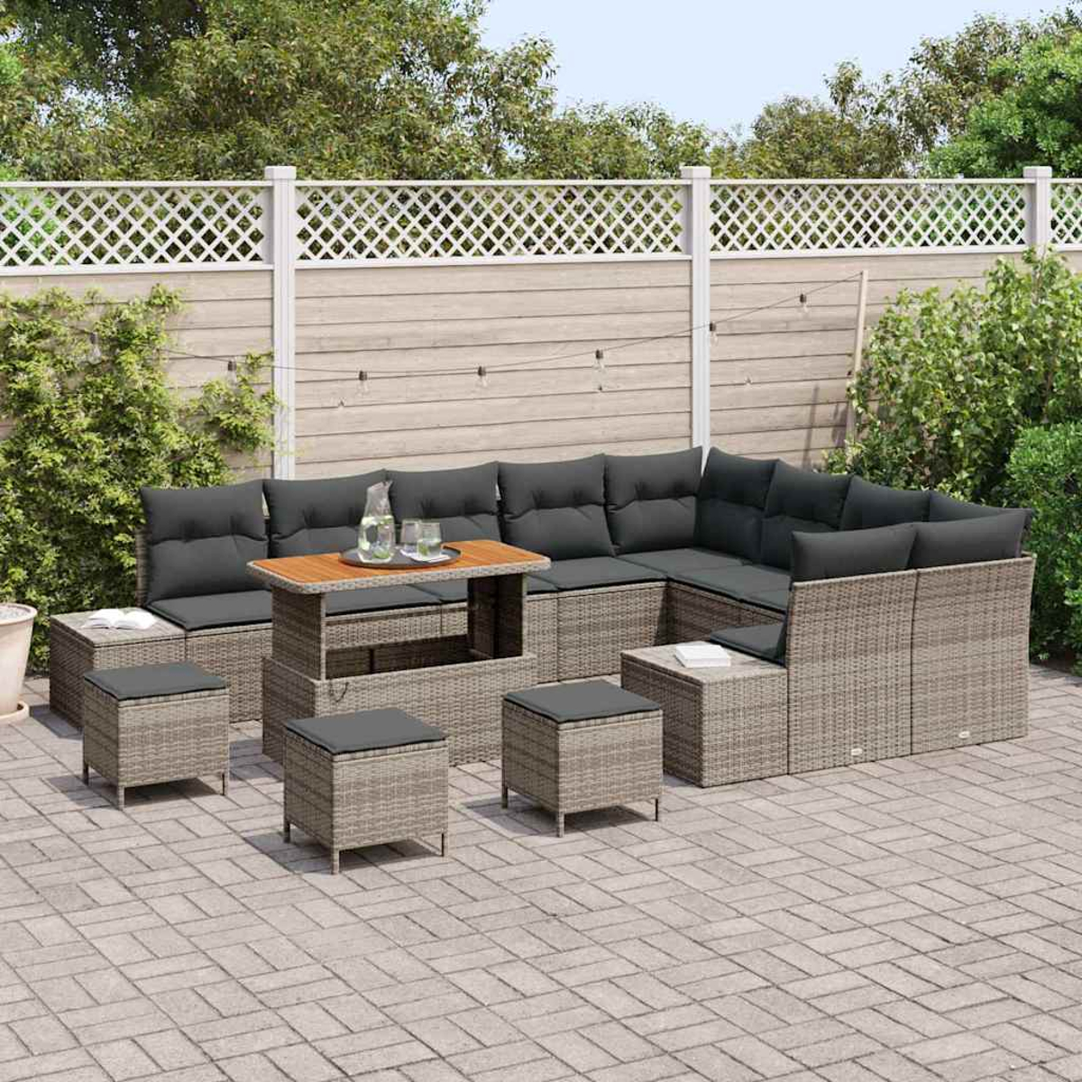 Outdoor-Ecksofa mit Kissen, Ottomanen und einem Tisch auf einer Terrasse. Im Hintergrund ein weißer Zaun und Grün.