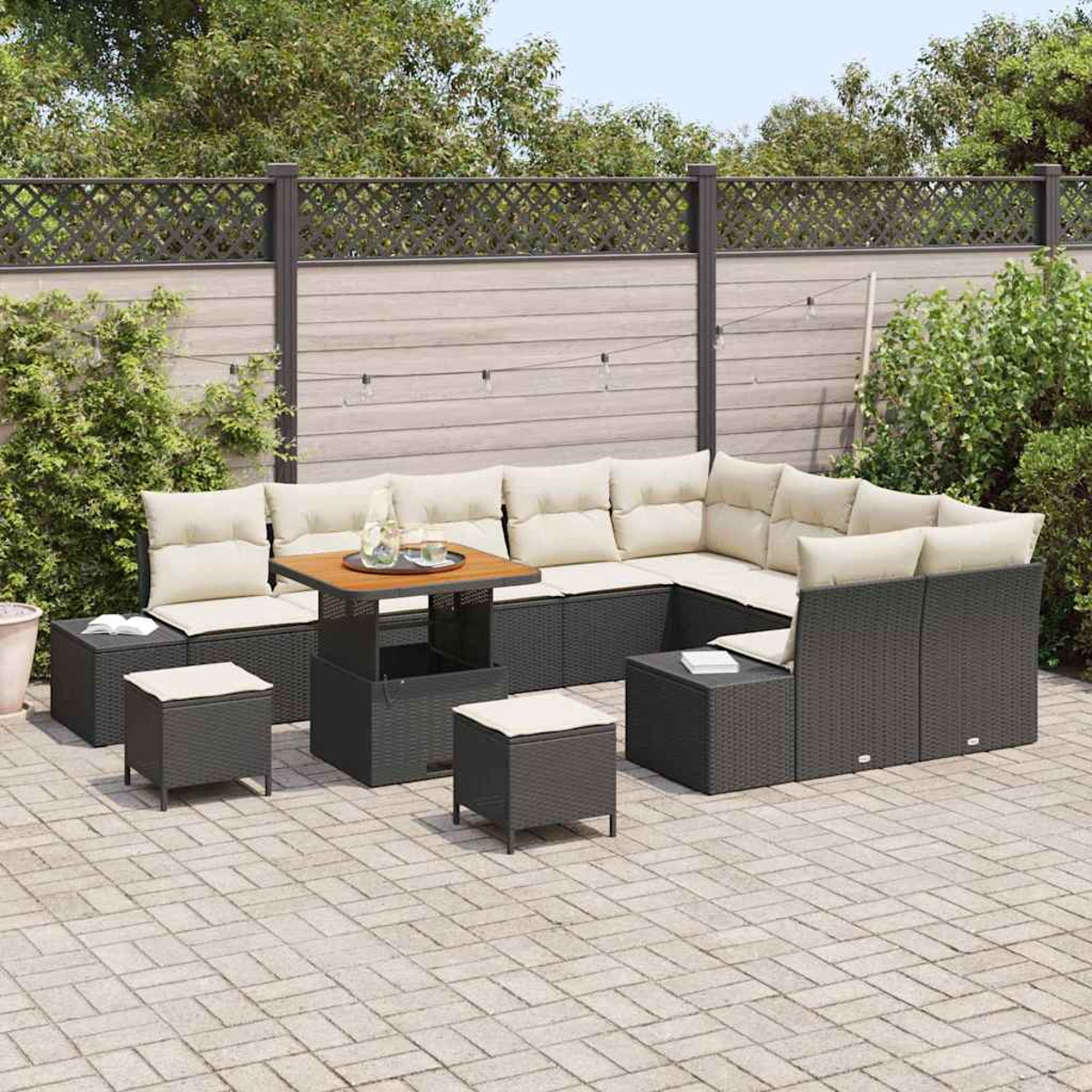 Seccional exterior con cojines beige, mesa con bebidas y dos otomanas en un patio de piedra. Valla y vegetación al fondo.