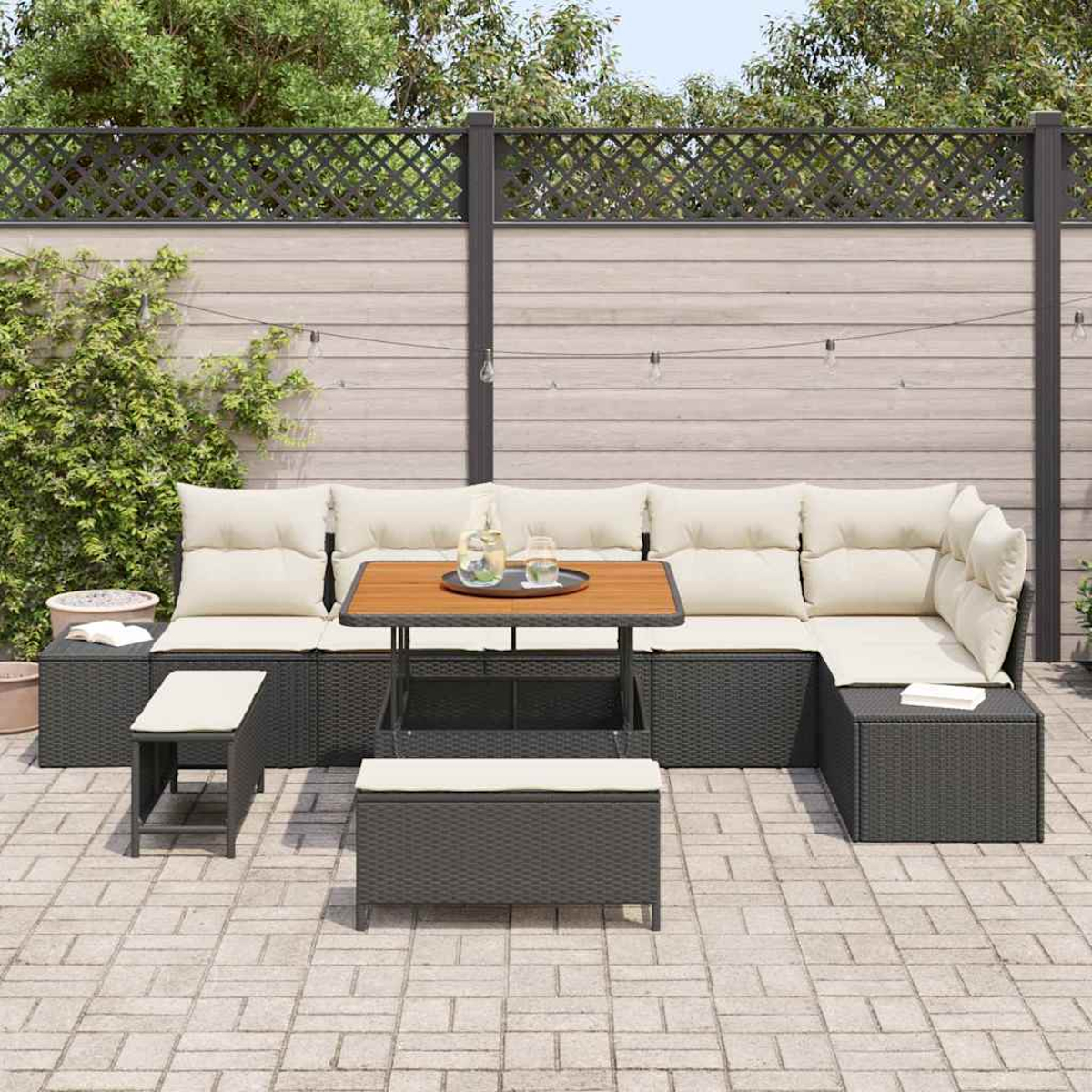 Garten-Terrassenset mit Sofa, Tisch und Bänken. Beige Kissen, dunkelgrauer Rahmen, Holztisch. Im Hintergrund ein Zaun und Grün.