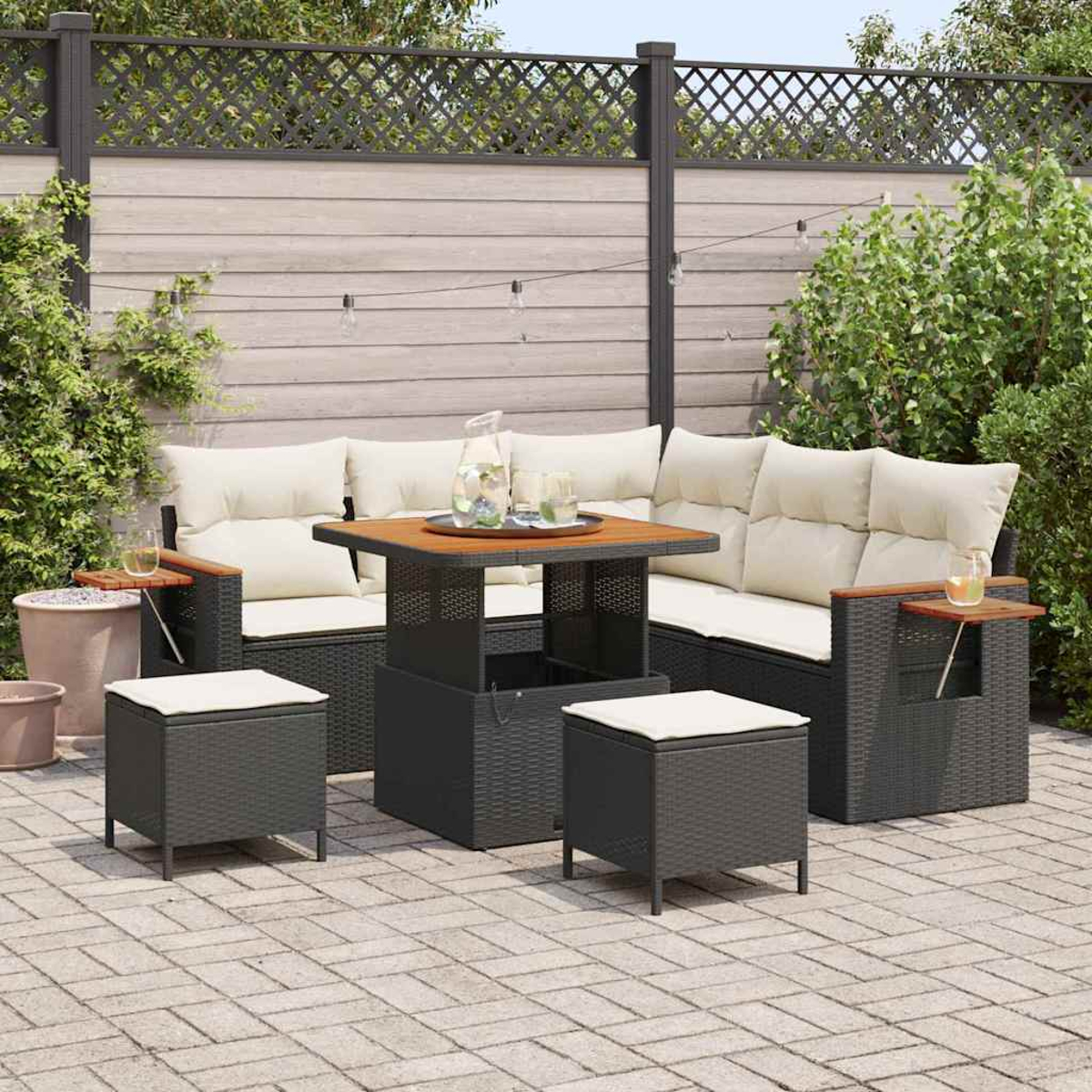 Garten-Terrassenset mit grauen Korbmöbeln, beigen Kissen und einem Holztisch. Enthält ein Sofa, zwei Ottomane und einen Tisch. Pflanzen im Hintergrund.