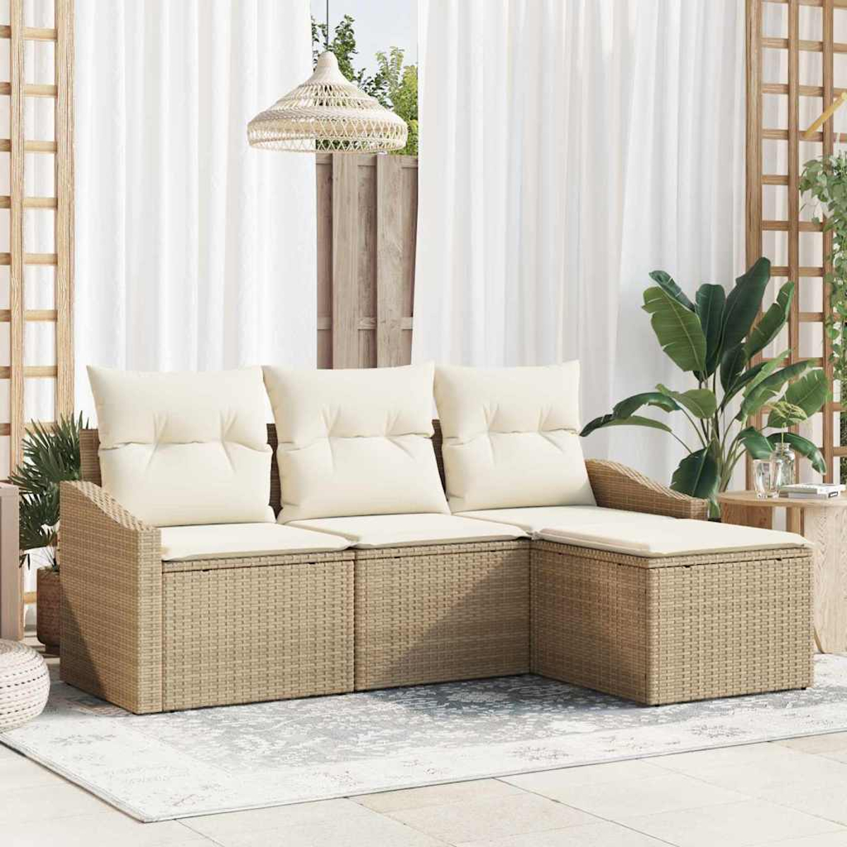 Sofá seccional exterior de mimbre con cojines crema. Detrás, cortinas blancas y una lámpara colgante. Plantas y una alfombra completan la escena.