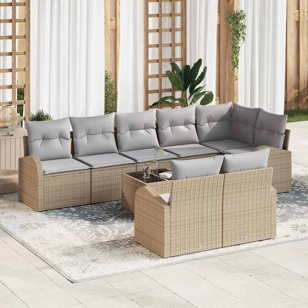 Rattan-Sofa-Set im Freien mit grauen Kissen, einem Tisch mit Glasplatte und einem gemusterten Teppich. Weiße Vorhänge und Holzstruktur im Hintergrund.