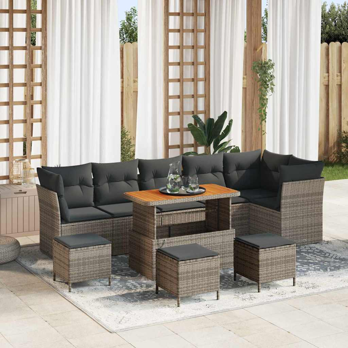Gartenmöbel mit Ecksofa, Ottomanen und Tisch. Kissen sind grau, Möbel im Korbstil. Vorhänge und Holzzaun im Hintergrund.