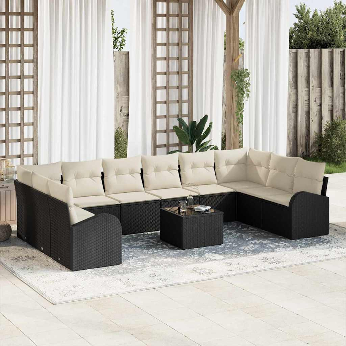 Una zona de estar al aire libre con un sofá seccional de mimbre negro y cojines crema. Una mesa cuadrada en el centro. Cortinas blancas al fondo.