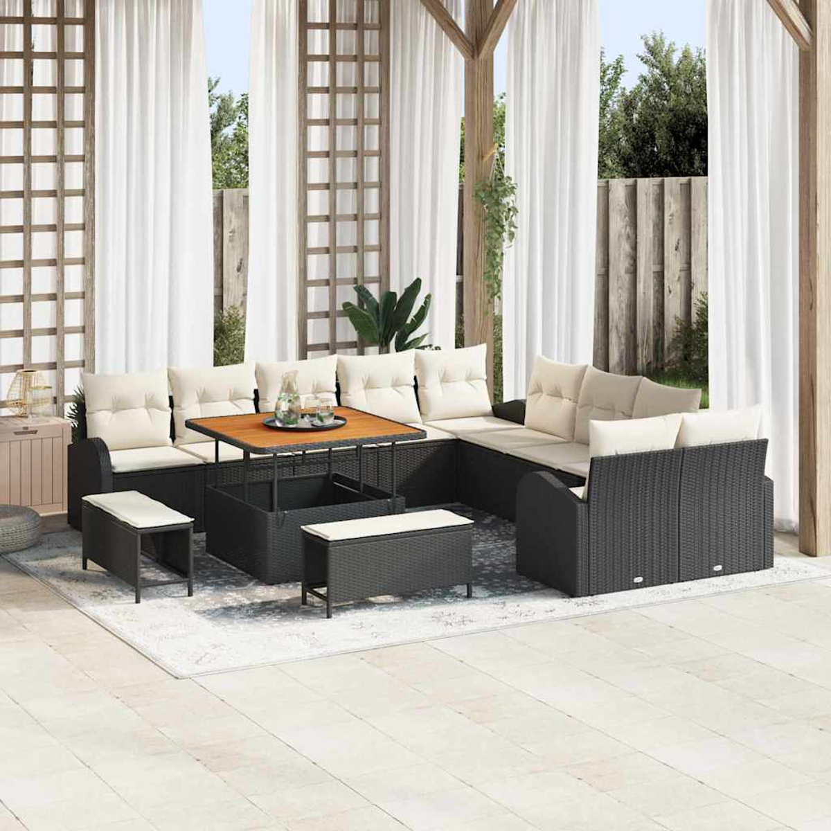 Garten-Sitzgruppe mit schwarzen Korbmöbeln, cremefarbenen Kissen und einem Holztisch. Weiße Vorhänge und eine Holzkonstruktion im Hintergrund.