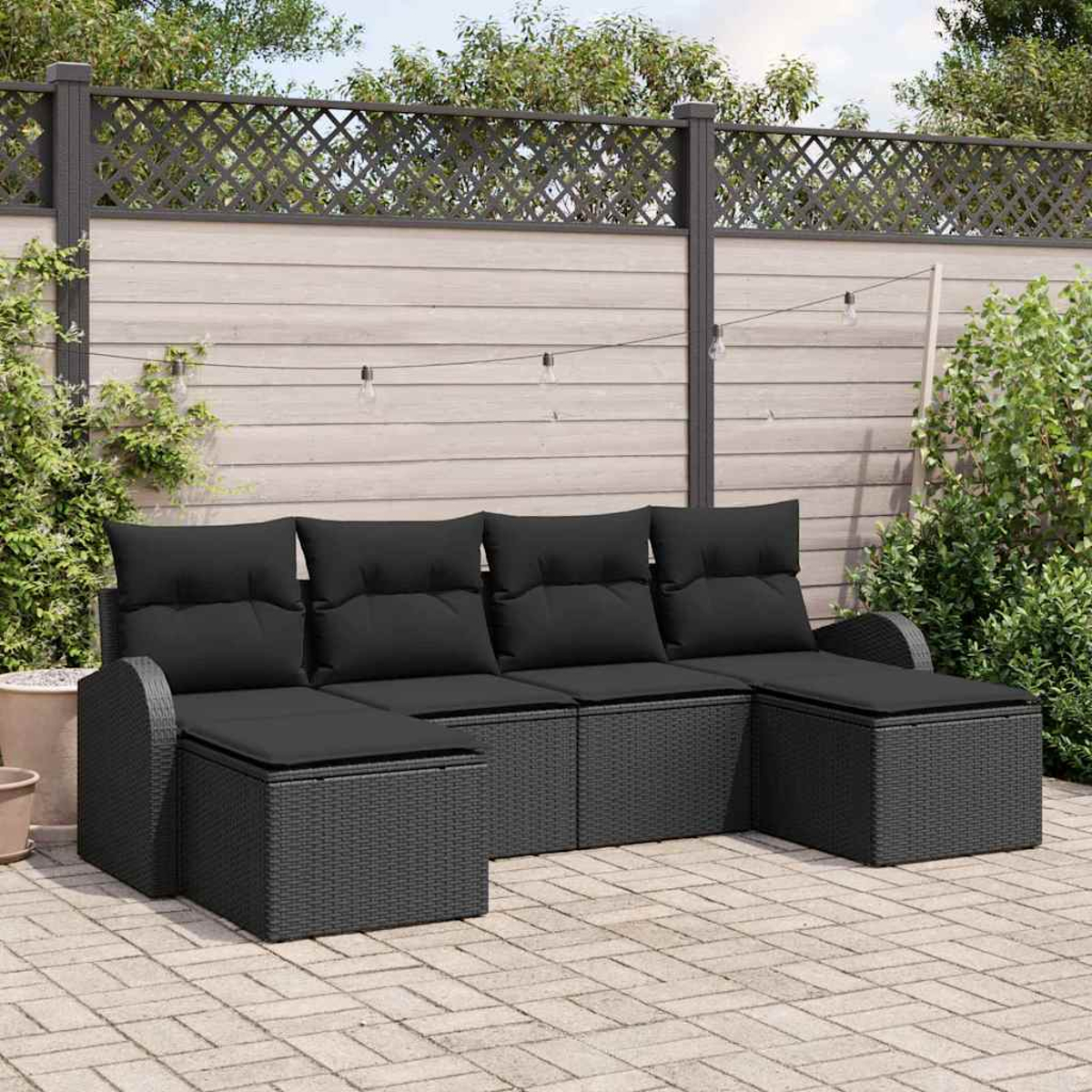 Schwarzes Outdoor-Ecksofa auf einer Backstein-Terrasse. Im Hintergrund ein Holzzaun und Grün.
