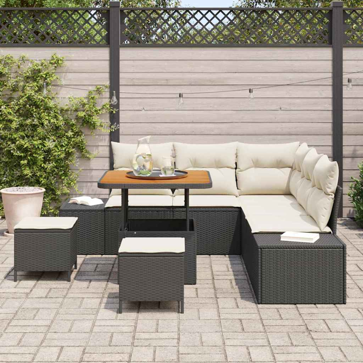 Outdoor-Ecksofa mit Kissen, einem Tisch mit Getränken und zwei Ottomanen. Im Hintergrund ein Zaun und eine Topfpflanze.