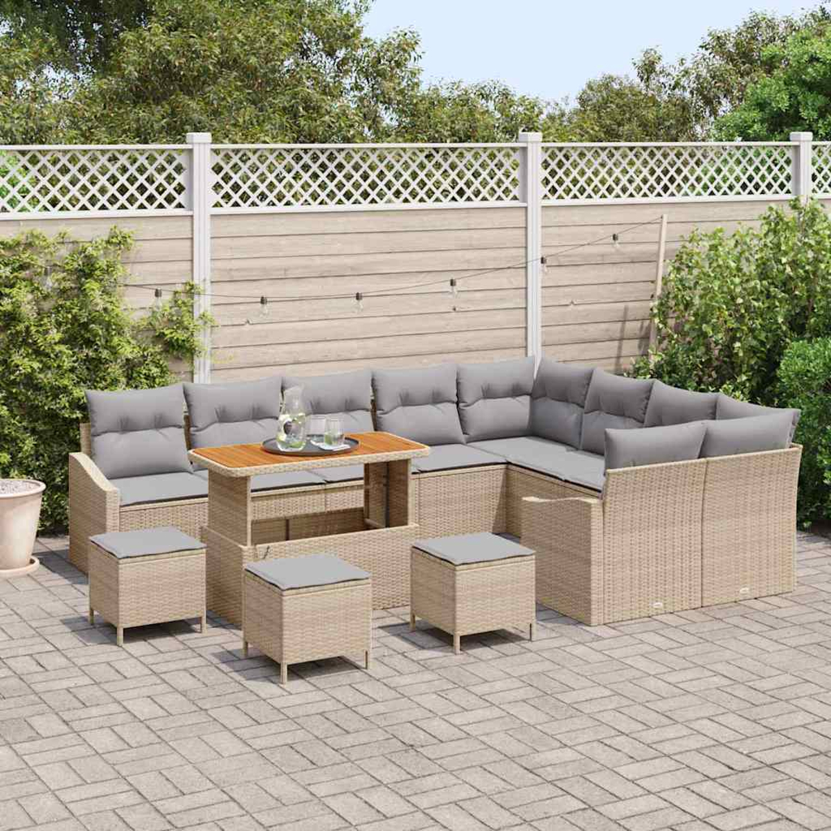 Outdoor-Terrassenmöbel-Set mit beigefarbenen Korbsesseln, grauen Kissen und einem Holztisch. Inklusive Ottomanen. Vor einem Zaun und Grün.