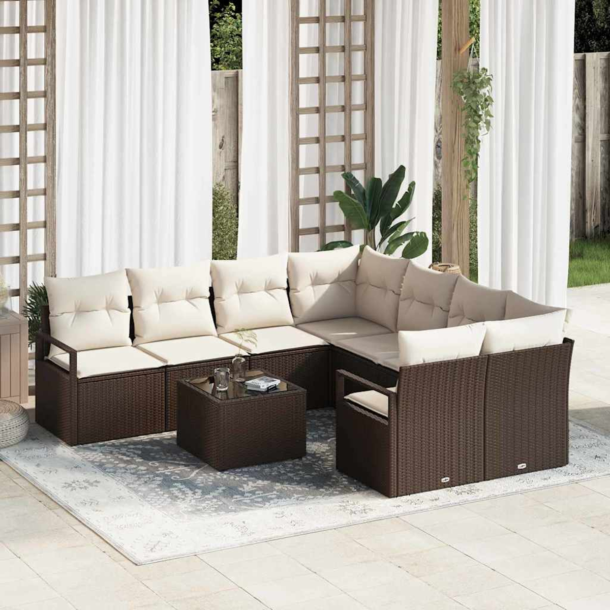 Outdoor-Ecksofa mit cremefarbenen Kissen und braunem Korbgeweberahmen auf einem gemusterten Teppich. Weiße Vorhänge und Spalier im Hintergrund.
