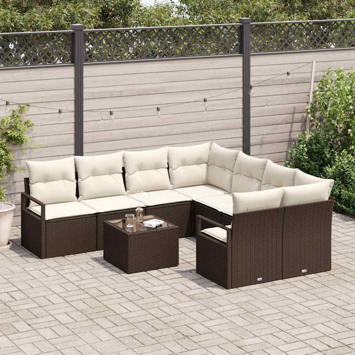 Outdoor-Ecksofa mit cremefarbenen Kissen und einem braunen gewebten Rahmen. Davor steht ein kleiner Tisch mit Gläsern. Im Hintergrund ein Zaun und Grün.
