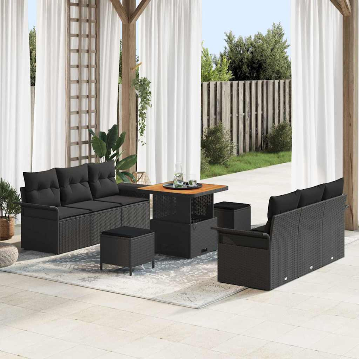 Terrassenset mit schwarzen Korbsesseln, Ottomanen und einem Tisch. Weiße Vorhänge und ein Zaun im Hintergrund.