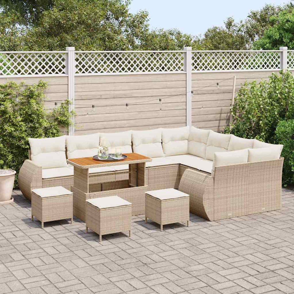 Garten-Terrassenset mit beigen Möbeln, weißen Kissen und einem Holztisch. Auf einer Backstein-Terrasse mit weißem Zaun und Grün.