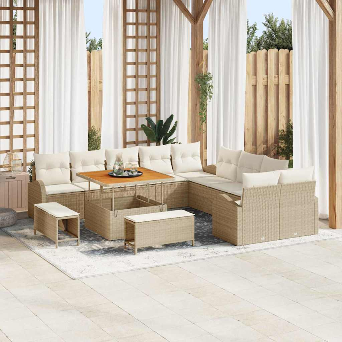 Set da patio all'aperto con mobili in vimini beige, cuscini bianchi, un tavolo di legno e tende bianche. Sono visibili anche un tappeto e una recinzione di legno.