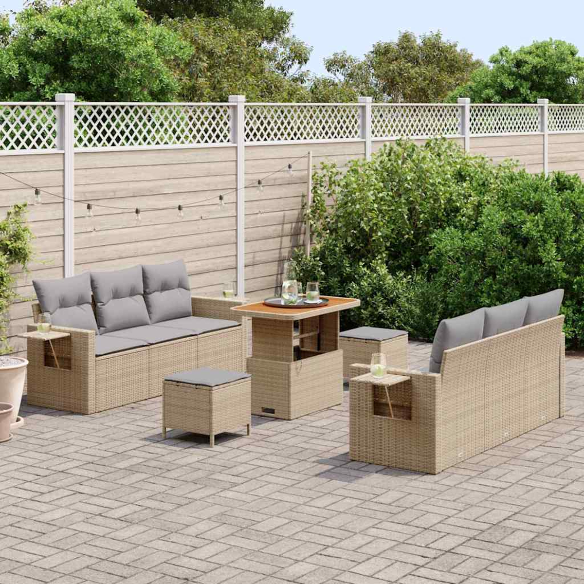 Garten-Terrassenset: zwei Sofas, ein Tisch und zwei Ottomane auf einer Backstein-Terrasse. Das Set befindet sich neben grünen Büschen und einem weißen Zaun.