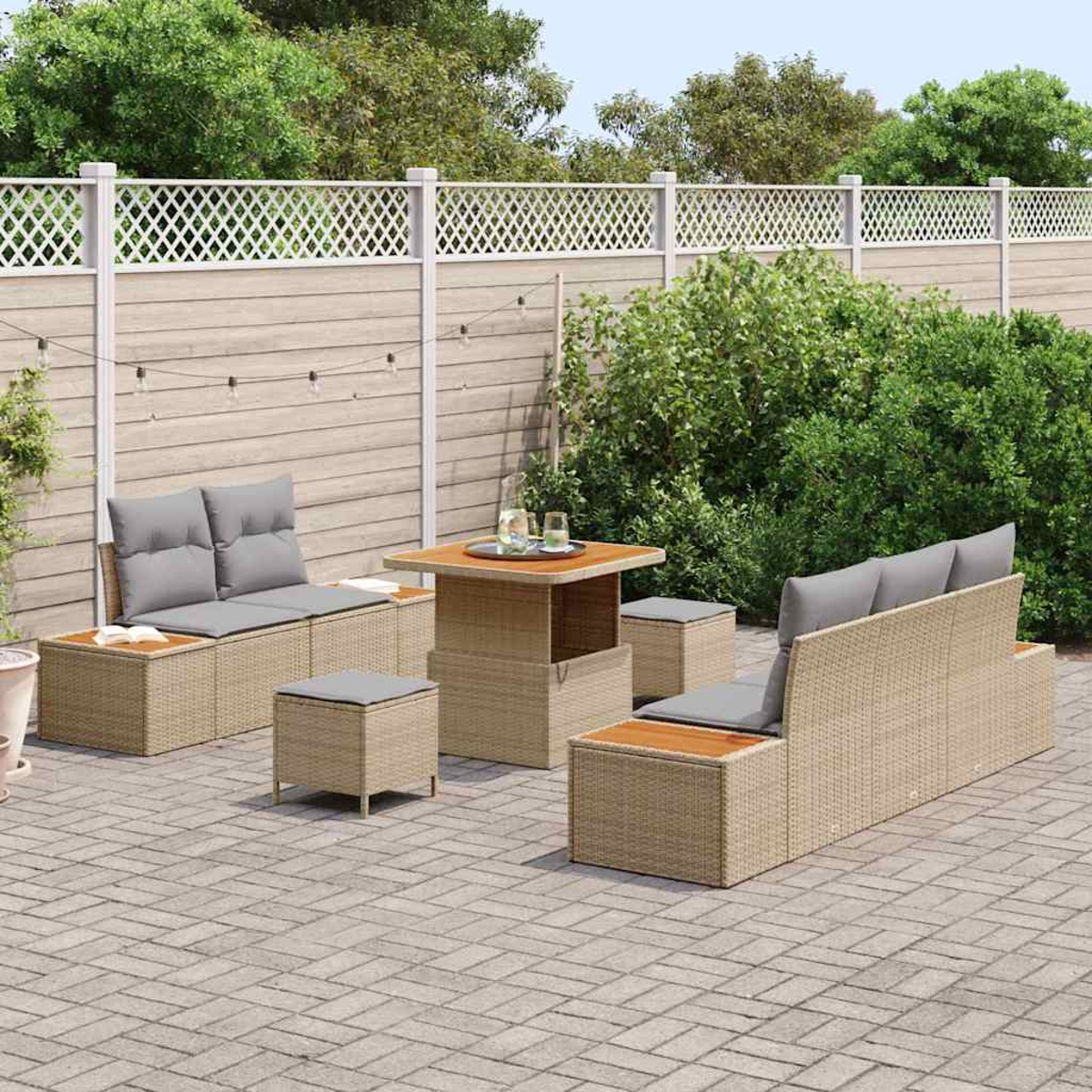 Garten-Terrassenset mit beigen Korbmöbeln und grauen Kissen. Enthält einen Tisch, Sitzgelegenheiten und Hocker. Vor einem Zaun und Grün.
