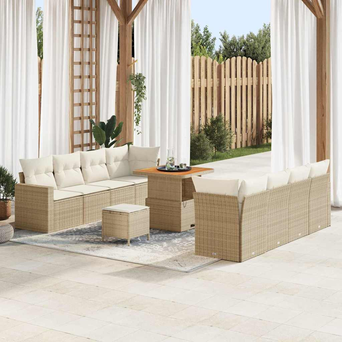 Terrassenset im Freien mit beigen Korbmöbeln, weißen Kissen und Vorhängen. Ein Holzzaun und Grünzeug im Hintergrund.