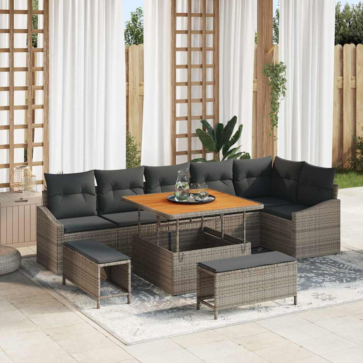 Gartenmöbel-Set: graues Korbsessel-Sofa mit schwarzen Kissen, Holztisch, zwei Bänken, auf einem Teppich. Weiße Vorhänge und Holzgitter.