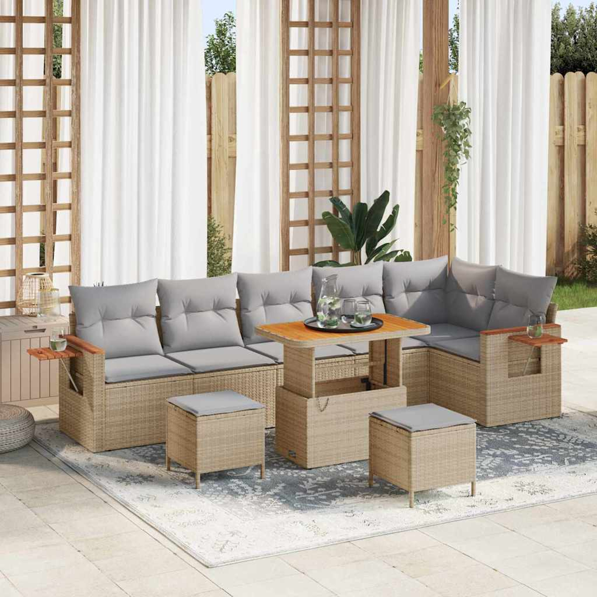 Divano in rattan da esterno con cuscini grigi, un tavolo in legno con bevande e due pouf. Tende e una recinzione in legno sullo sfondo.