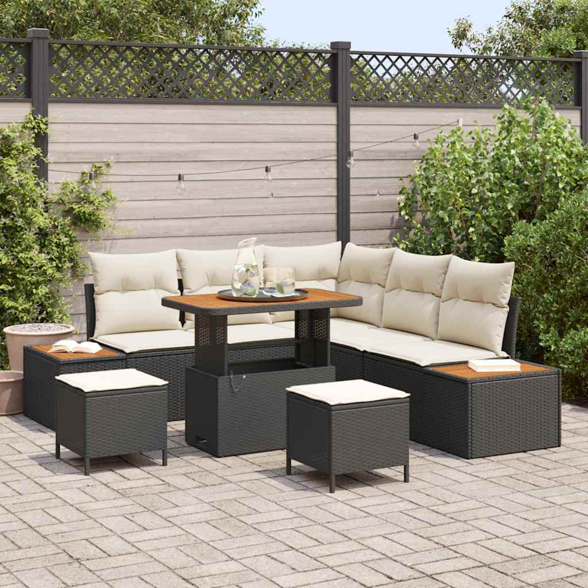 Terrassengarnitur mit Sofa, Tisch und Hockern. Beige Kissen auf dunkelgrauen Möbeln. Tischplatte aus Holz. Hintergrund: Grün und Zaun.