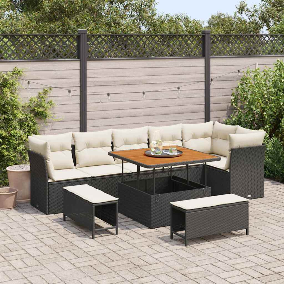 Outdoor-Sitzgruppe mit grauem Korbsessel, Holztisch und Bänken auf einer Ziegelterrasse mit Holzzaun.