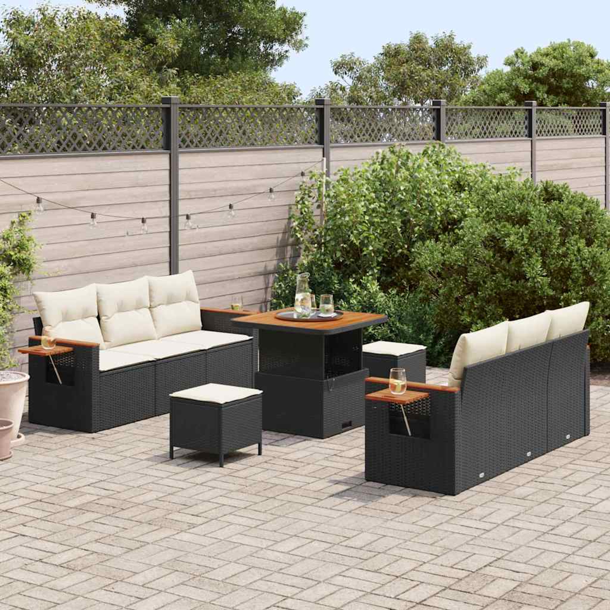 Terrassenset mit schwarzen Korbmöbeln, beigen Kissen und einem Holztisch auf einer Backsteinterrasse mit Zaun im Hintergrund.