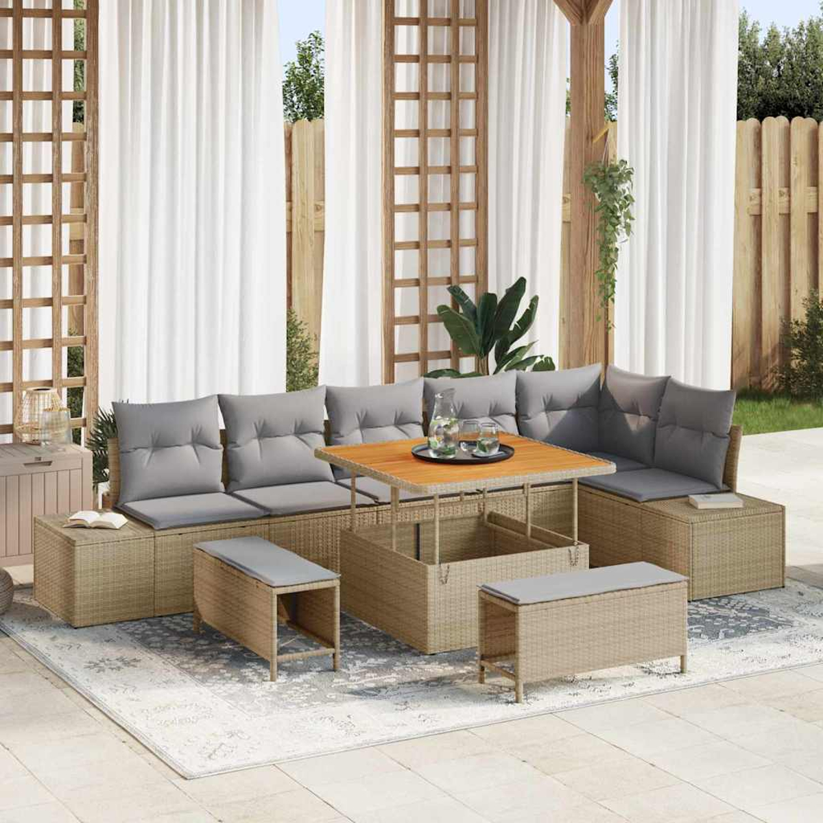 Outdoor-Rattansofa-Set mit grauen Kissen, Holztisch und Bänken auf einem gemusterten Teppich, vor weißen Vorhängen und einer Holzkonstruktion.