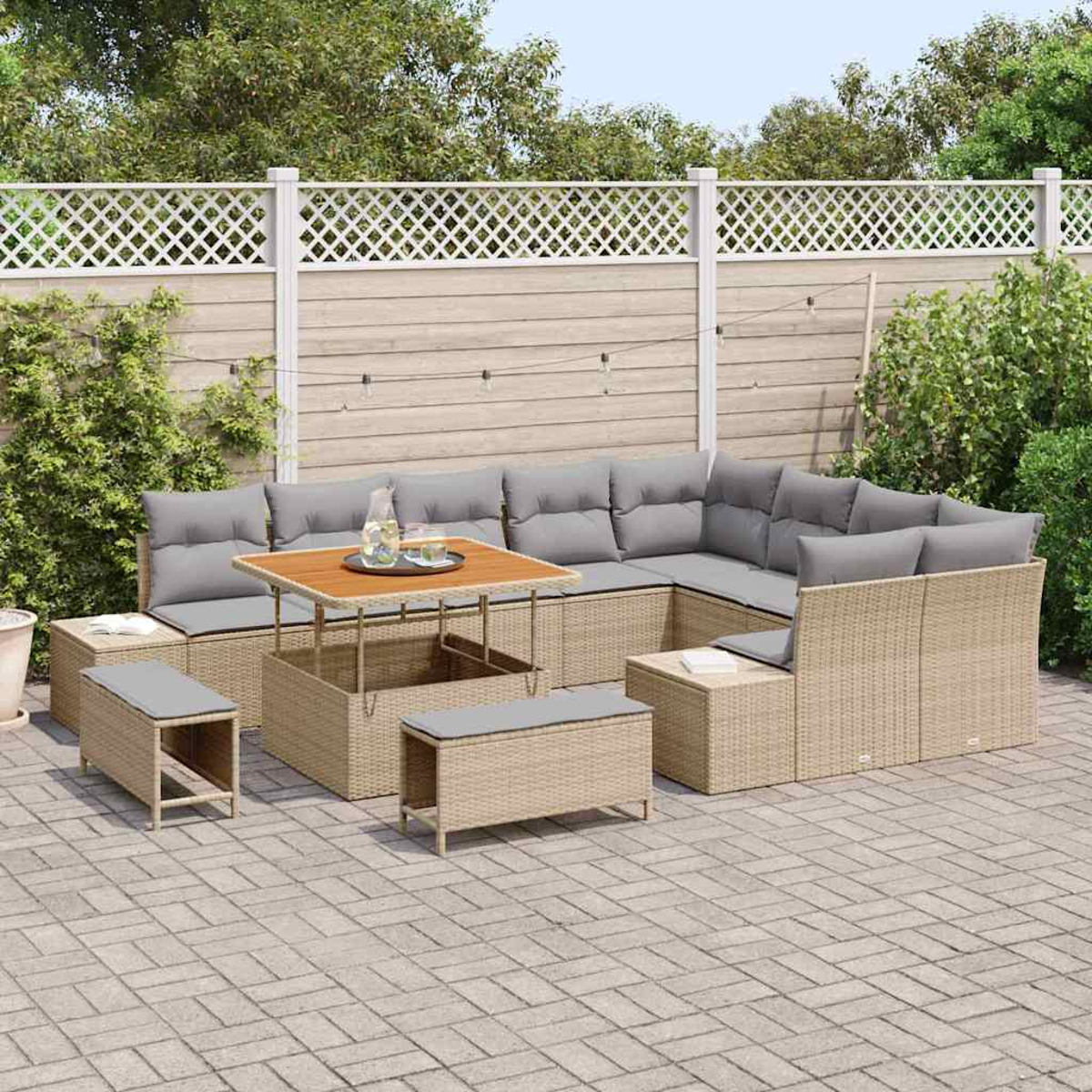 Gartenmöbel-Set. Beigefarbenes Wicker-Ecksofa, Tisch und Bänke mit grauen Kissen, auf einer gepflasterten Terrasse, mit einem Zaun im Hintergrund.