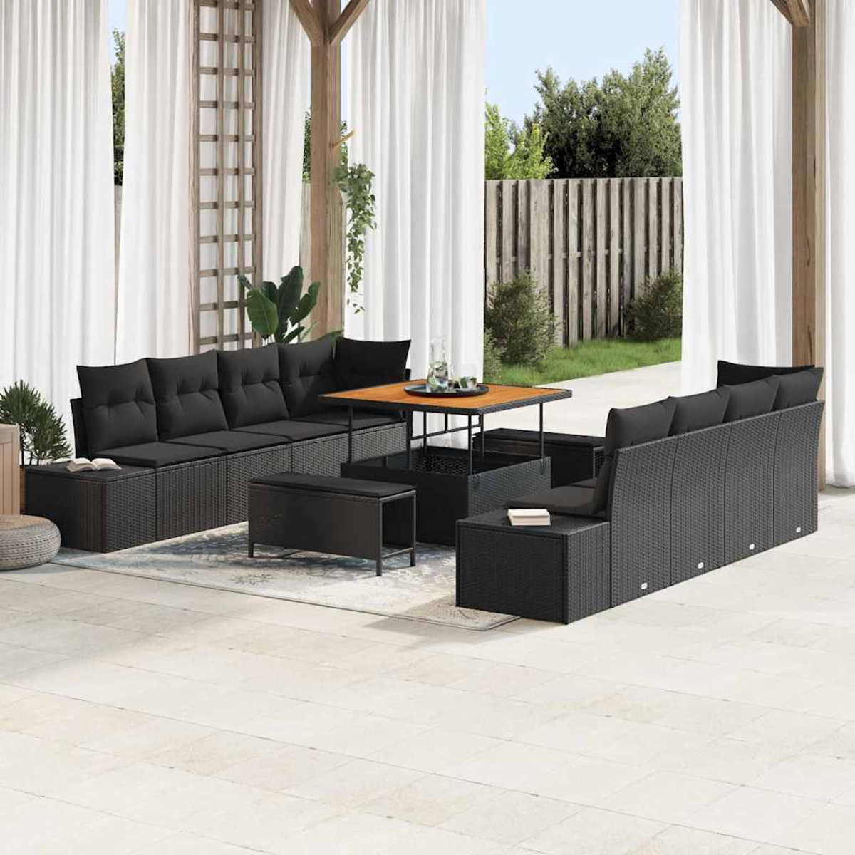 Garten-Sitzgruppe mit schwarzen Kissen und einem Holztisch. Auf einer Terrasse mit weißen Vorhängen und Holzzaun im Hintergrund.