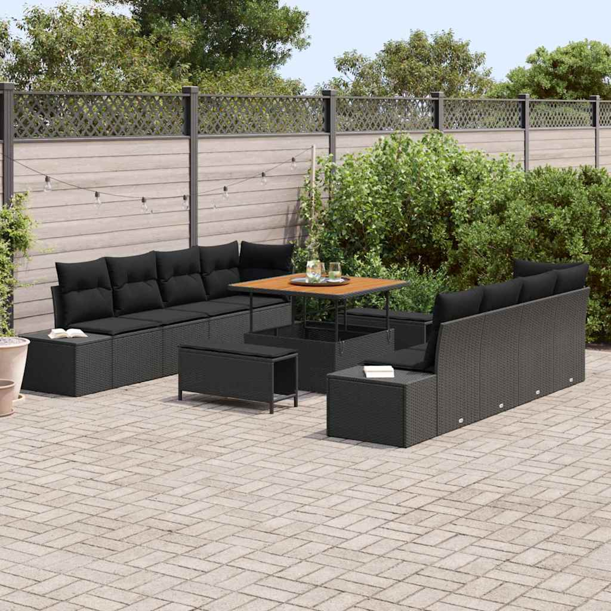 Gartenmöbel-Set. Schwarze Korbsessel und eine Bank umgeben einen Holztisch. Grüne Büsche und Holzzaun im Hintergrund.