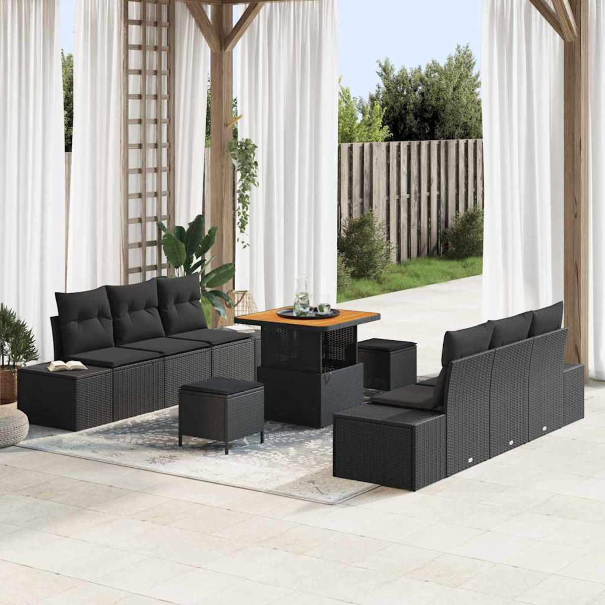 Gartenmöbel-Set, schwarzes Geflecht mit schwarzen Kissen, Tisch, Hocker und Sofa unter einer Holzpergola. Weiße Vorhänge im Hintergrund.