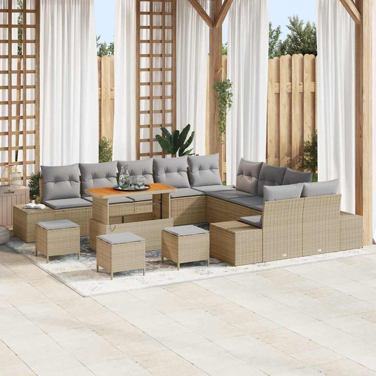 Juego de patio al aire libre con muebles de ratán, cojines grises y mesa de centro de madera. Cortinas blancas, valla de madera y plantas verdes.